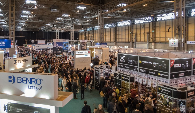 Visitors walking the aisles between exhibitor stands in a large exhibition hall